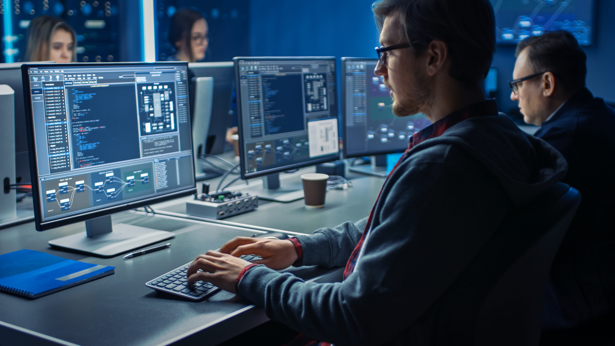 Two men and two women sit opposite each other, programming sophisticated code on wireless keyboards and looking at monitors.