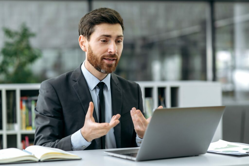 Insurance broker sits at desk discussing a Cyber Insurance policy form with a business client via laptop computer video conference. 