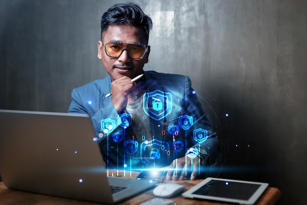 Cyber Insurance broker sits at desk with laptop and tablet computers, reviewing state of Cyber Insurance market. 