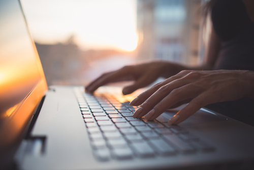 Close-up of a woman’s hands typing on a laptop keyboard. 