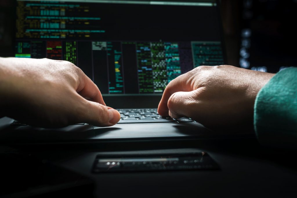 Close up of a man’s hands as they type digital code into a black laptop.