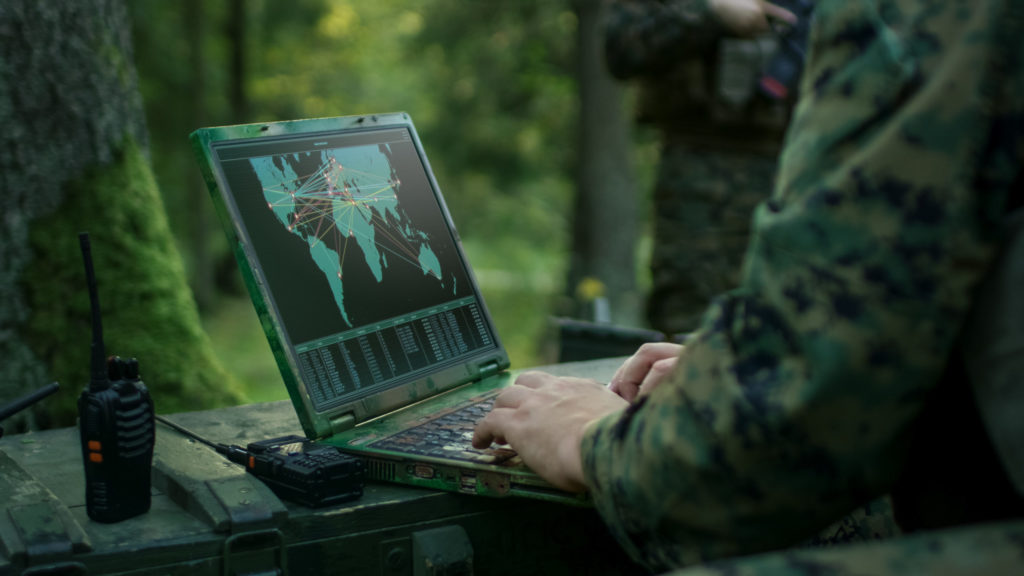 Soldier in the woods on his laptop as he hacks into enemy systems.