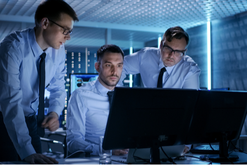 Three network security professionals in business attire are working to set up security in the system control room. 